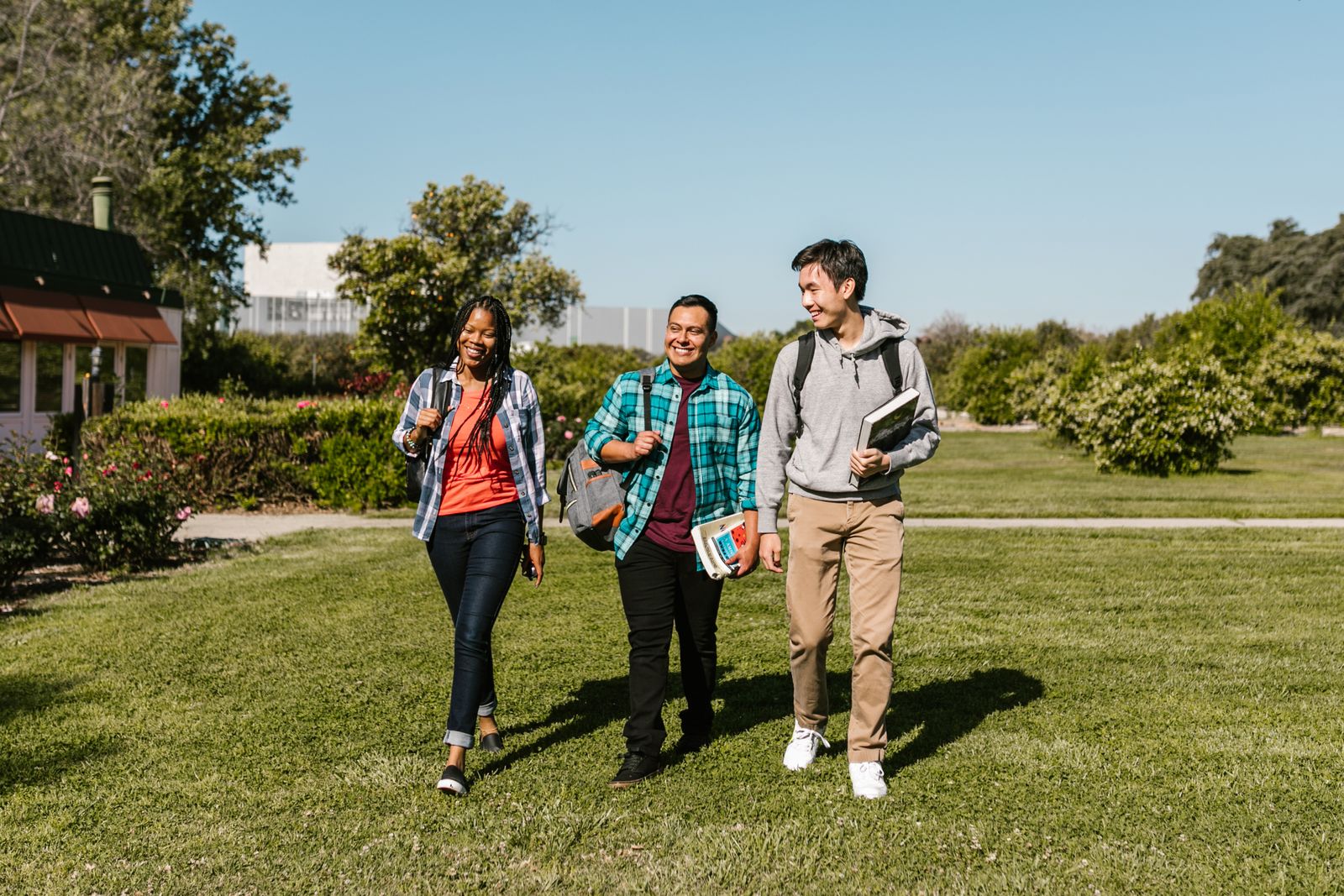 Estudiantes internacionales caminando juntos en el parque de un campus universitario soleado